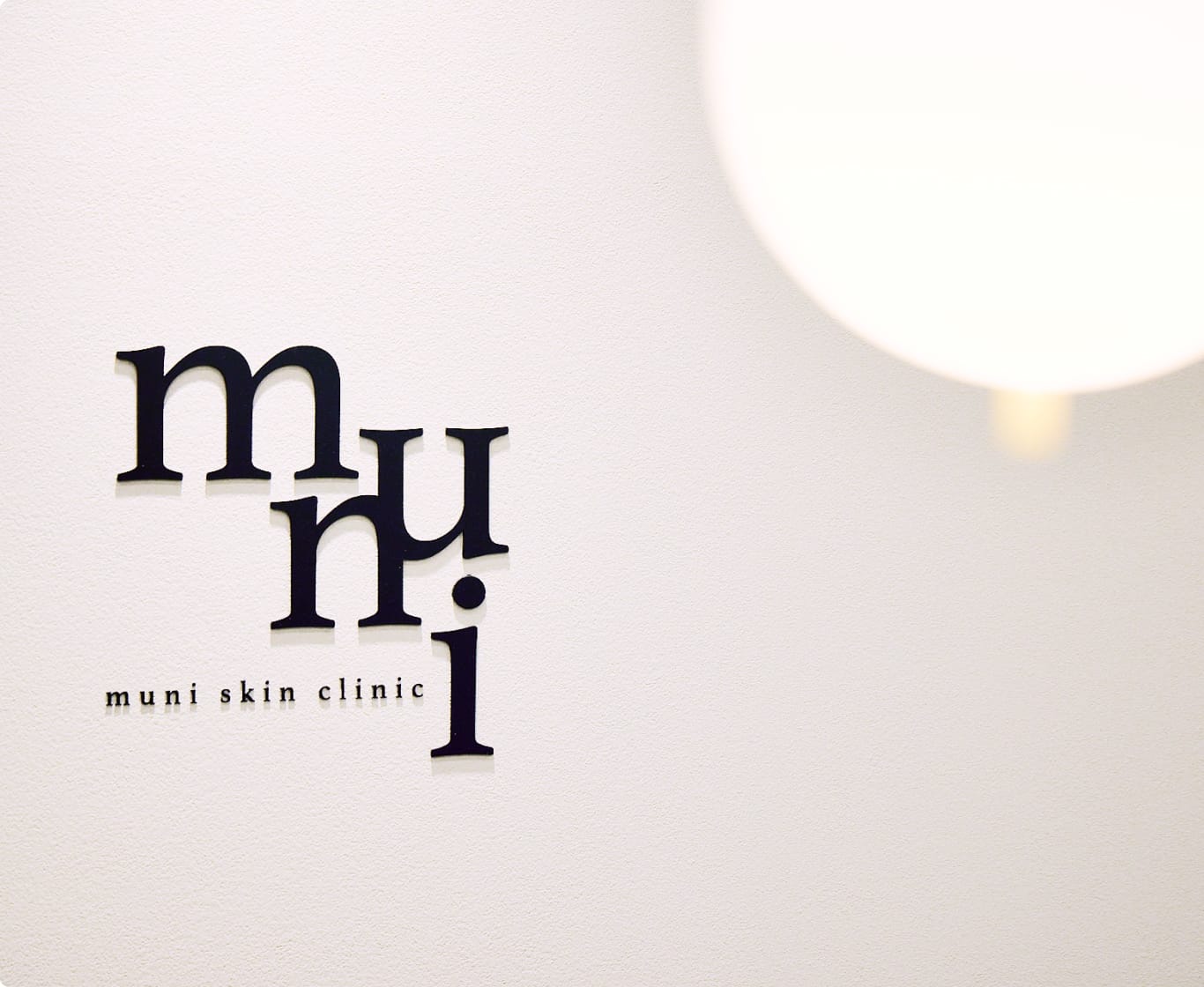 白い壁に「muni skin clinic」のロゴが黒い立体文字でデザインされている